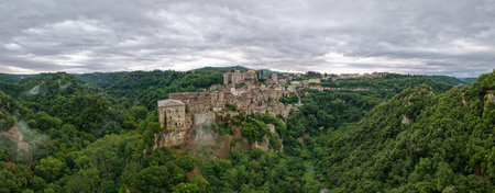 Aerial view of Sorano, Italy, showcasing medieval architecture nestled in lush Tuscan hills. Stone...