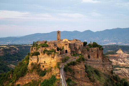 Civita di Bagnoregio, a picturesque hilltop village in Italy, bathed in soft morning light with surrounding lush greenery and clear skies.の写真素材