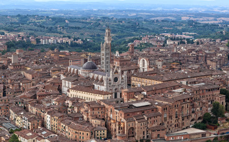 Gothic Siena Cathedral features black and white marble stripes, iconic Romanesque facade, with towering campanile against Tuscany's rolling landscapes.の写真素材