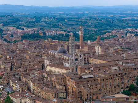 The Gothic Siena Cathedral, crafted from white and green-black marble, dominates the historic skyline of Siena, Italy, with intricate facades and a towering bell tower.の写真素材