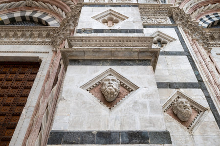 Siena, Italy - Jul 19, 2025: Gothic facade of Siena Cathedral with white and dark marble stripes, sculpted heads, and intricate arches.の写真素材