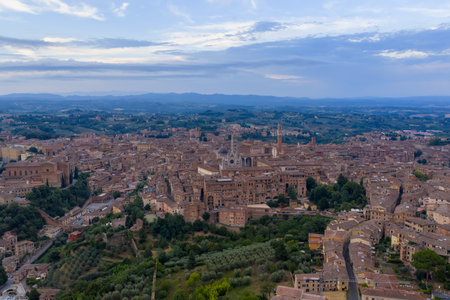 Aerial view of Siena, Italy, highlights medieval architecture with red-tiled roofs and narrow streets. The city, renowned for its Gothic style, glows under a pastel twilight sky.の写真素材