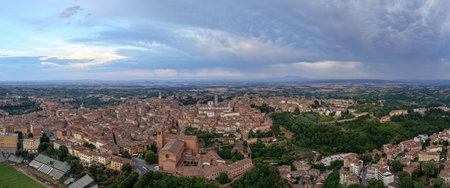 Aerial view of Siena, Italy, showcasing medieval brick buildings, the iconic Torre del Mangia, and the Siena Cathedral. Rolling Tuscan countryside under dramatic cloud-filled skies.の写真素材