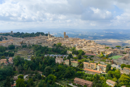 Aerial view of medieval Volterra, Tuscany, showing stone houses, church towers and surrounding countryside under a partly cloudy summer sky.の写真素材