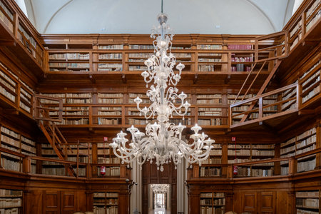 Mantua, Italy - Jul 26, 2025: Interior of the 18th-century Biblioteca Teresiana in Mantua, Italy, showing wooden book galleries and ornate white chandelier under vaulted ceiling.の写真素材
