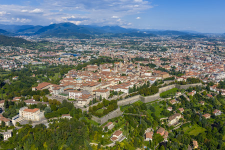 Aerial view of Bergamo residential hillsides and dense urban fabric, surrounded by green slopes and distant Alpine foothills under summer light.の写真素材