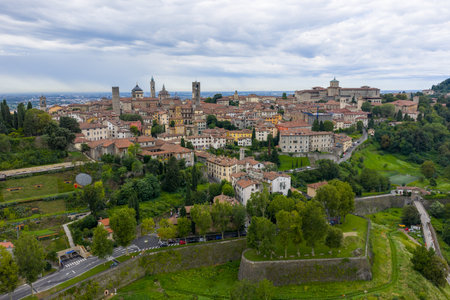 Drone panorama of Bergamoâs CittÃ  Alta showing medieval skyline and UNESCO-listed Venetian defensive walls above terraced greenery under cloudy skies.の写真素材