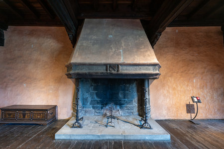 Fenis, Italy - Aug 2, 2025: Medieval stone fireplace in FÃ©nis Castle, Valle dâAosta, showing Gothic interior with soot-darkened hearth and wooden chest on plank floor.の写真素材
