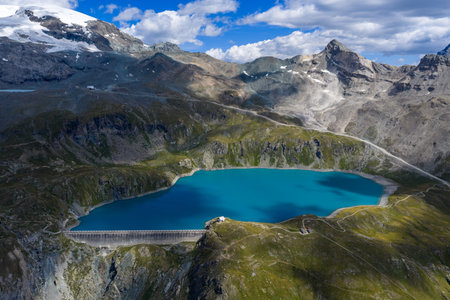 Aerial view of turquoise Lago Goillet reservoir above Valtournenche in the Aosta Valley Alps, surrounded by rocky peaks and summer meadows.の写真素材