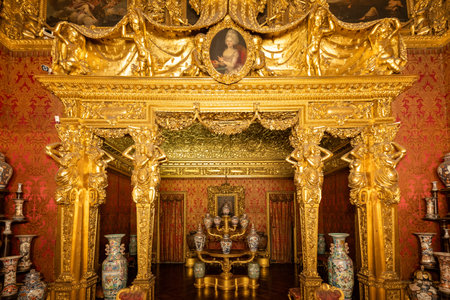 Turin, Italy - Aug 10, 2025: Baroque gilded salon in the Royal Palace of Turin featuring ornate stucco, portrait medallion, chinoiserie vases, and carved columns.の写真素材