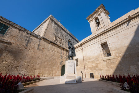 Bronze statue of Jean de Valette on a stone plinth in a limestone courtyard, framed by historic fortification walls and a bell tower in Valletta, Malta.の写真素材