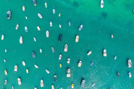 Top-down aerial view of small boats anchored in clear turquoise water at Marsaxlokk marina, Malta,...