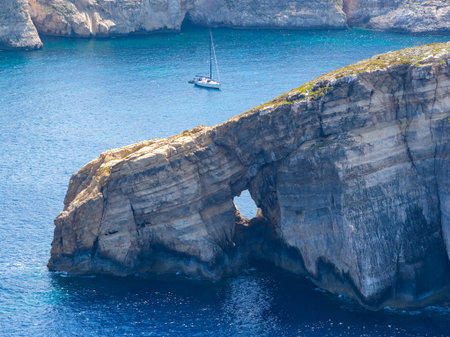 Limestone sea cliff at Dwejra Bay, Gozo, with a small natural arch and deep blue Mediterranean water under summer light.の写真素材