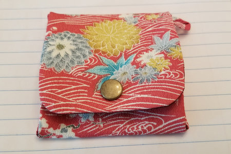 Red, blue, yellow, and white Japanese kanzashi hand made purse constructed from kimono material on an off-white lined backgroundの写真素材