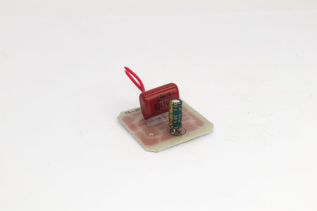 A PCB with two capacitors with a red wire.