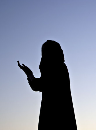 Girl silhouette with the extended hand in a raincoat on a background of the pre-dawn skyの写真素材