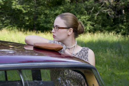 Beautiful girl in glasses at the car on a green wood backgroundの写真素材
