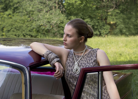Beautiful girl at the car on a green wood backgroundの写真素材