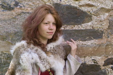 Portrait of the young girl in the Scandinavian historical suit on a ancient stone wall backgroundの写真素材