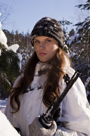 Sniper girl in white camouflage aiming with rifle at winter forest 