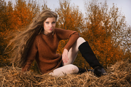 Pretty girl resting on straw bale on the autumn landscape backgroundの写真素材