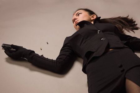 Detective scene imitation. Woman in a black suit with gun lying on the floorの写真素材