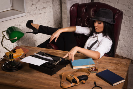 Retro detective girl sits at a table in the agencyの写真素材