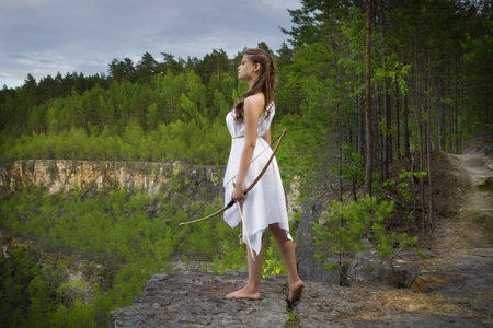 young girl shoots a bow from a high cliff in the forestの写真素材