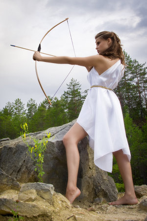 young girl shoots a bow from a high cliff in the forestの写真素材