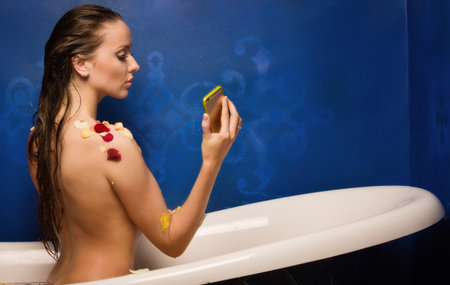 Beautiful sexy woman in bath with flowers petals while using the smart phone. she is doing a selfieの写真素材