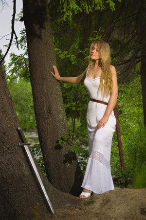Beautiful blond woman in white dress with sword in a wild forestの写真素材