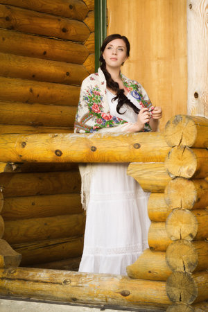 Russian woman in traditional clothes on background of the hut