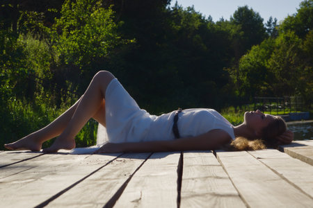 Relaxing young woman on wooden pier at the lake in summer dayの写真素材