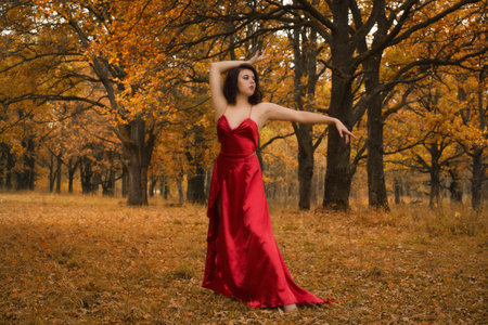 Girl in a long red dress dancing in the autumn forestの写真素材
