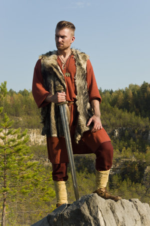 Viking with a sword on a cliff in the mountains