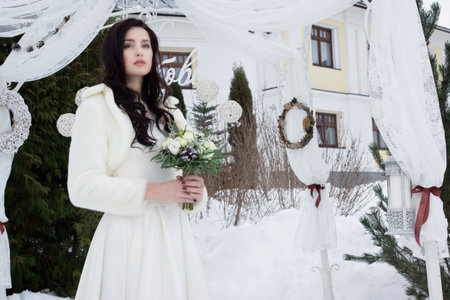 Beautiful bride in a fur cape with a bouquet of flowersの写真素材