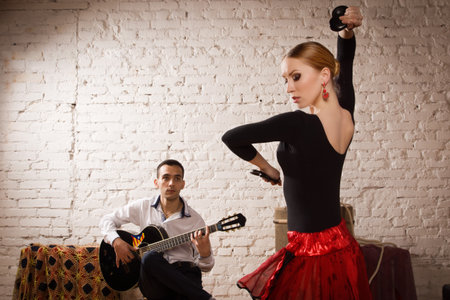 Young woman dancing flamenco in traditional flamenco dress and a man playing the guitarの写真素材