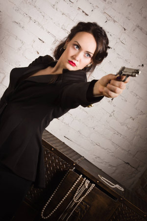Noir film style woman in a black suit posing with a gunの写真素材