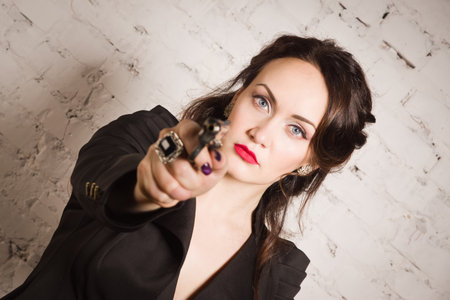 Noir film style woman in a black suit posing with a gunの写真素材