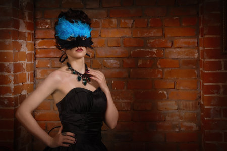 Sensual gothic woman in a long gorgeous black dress and mask at dark interiorの写真素材