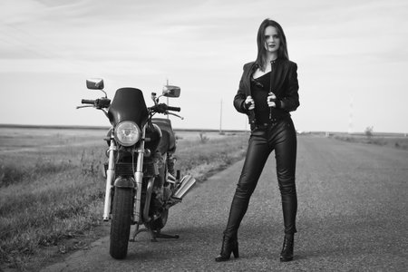 Sexy biker girl in a leather jacket posing near motorcycleの写真素材