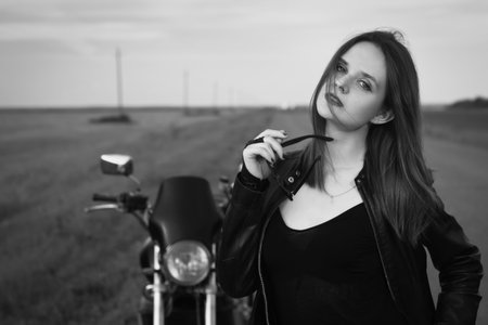 Sexy biker girl in a leather jacket posing near motorcycleの写真素材