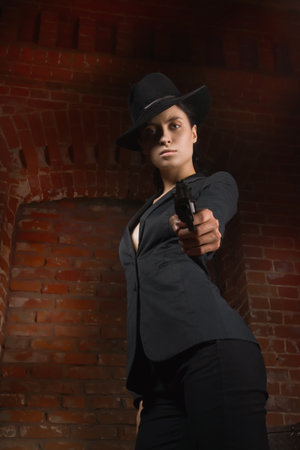 Noir film style woman in a black suit posing with a gunの写真素材