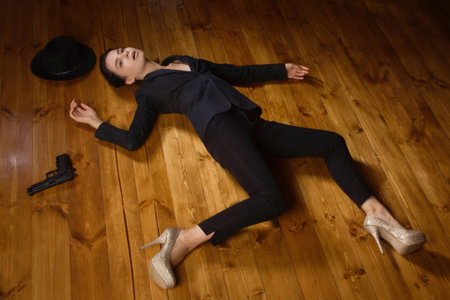 Detective scene imitation. Woman in a black suit with gun lying on the floorの写真素材