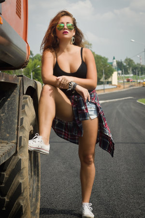 Fashionable sportive girl posing next to an excavator on a construction siteの写真素材