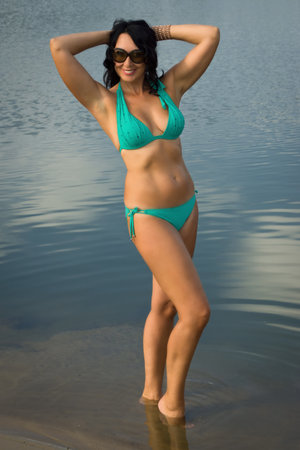 Beautiful adult woman in bikini relaxing on the beach by the lakeの写真素材