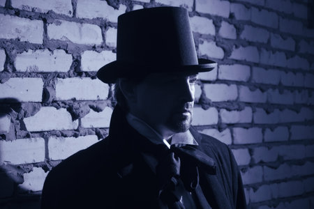 Victorian man in the black coat, top hat and in a tie on a wall backgroundの写真素材