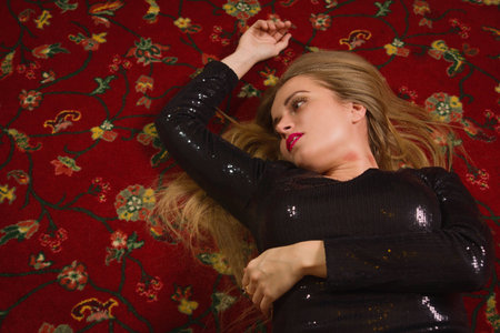 Strangled beautiful woman in a short black dress lies on the floor. Simulation of the crime scene.の写真素材