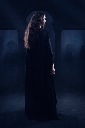 Beautiful naked gothic girl in a black cloak against a nightscape in the cemeteryの写真素材