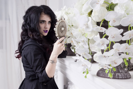 Sensual gothic woman in a long gorgeous black dress at white interior